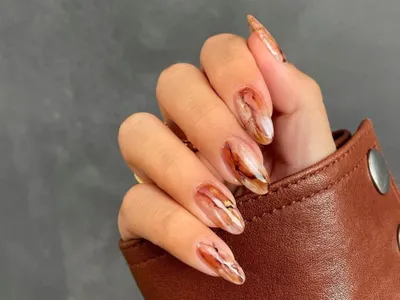 Close-up of hand with sheer brown marbled manicure and brown leather sleeve
